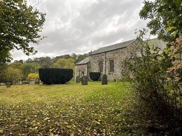 A stone building with a cemetery and trees
Description automatically generated